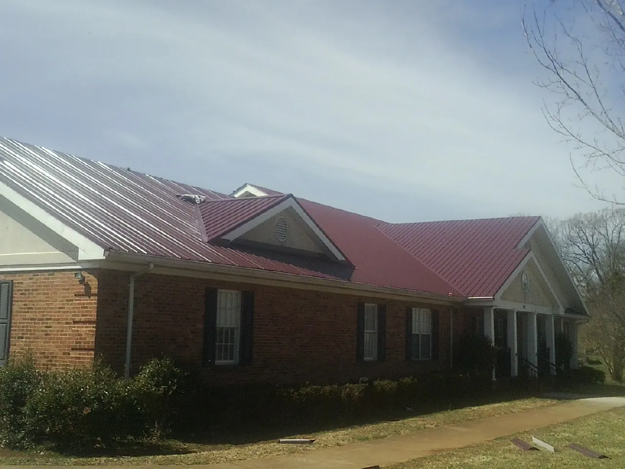 Red metal roof with gabled entries on a long brick building, from a Hail Damage Roof Repair job in Colchester