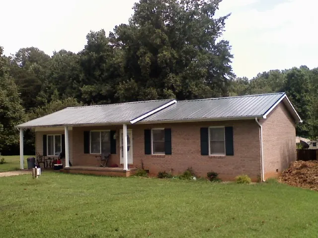 Gray metal roof on a brick ranch house with a side carport in Colchester