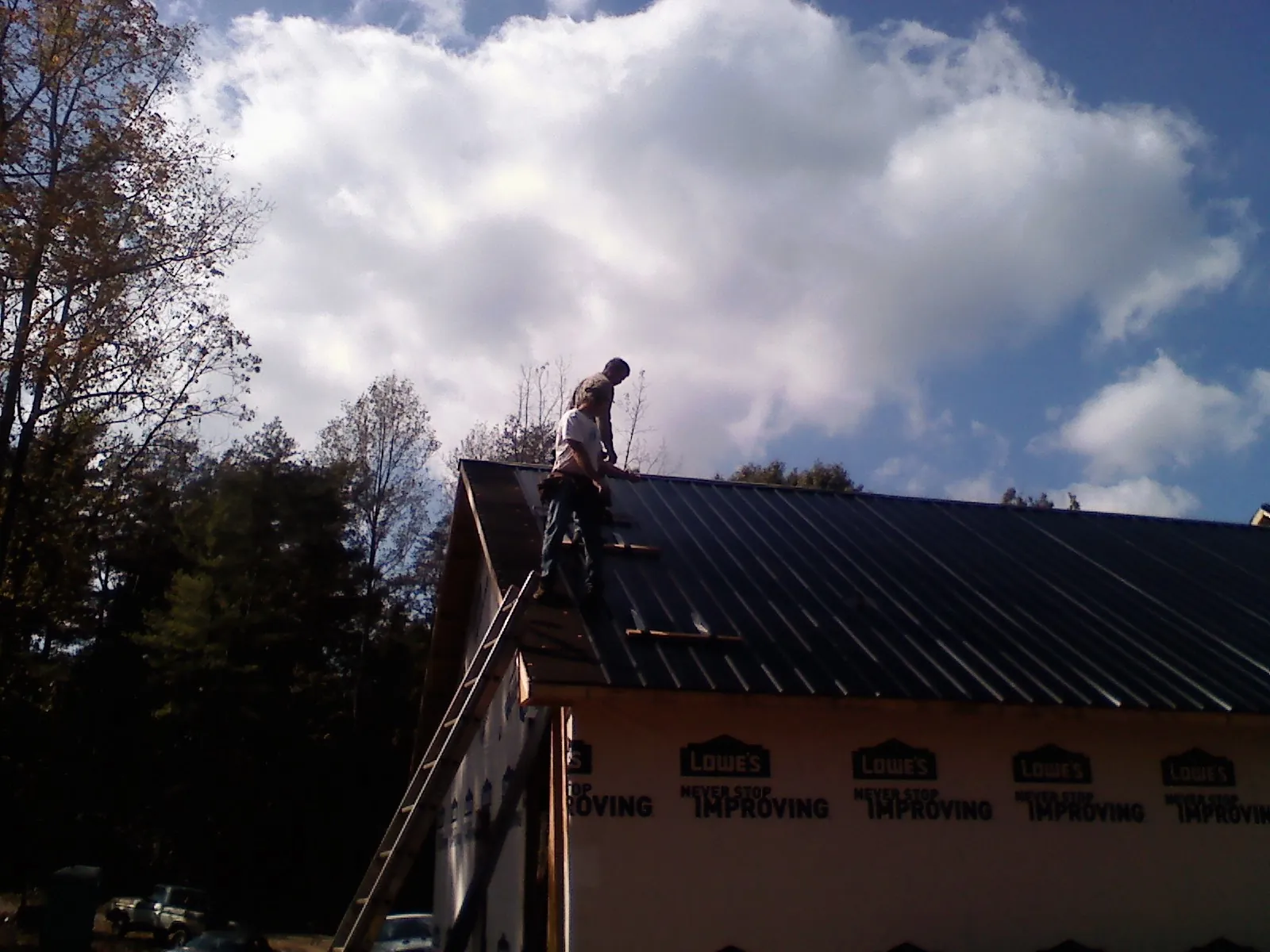 Roofer fastening dark metal panels high against a cloudy sky, from a Roof Inspection job in Colchester